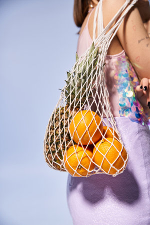 A young woman with brunette hair happily holds a bag full of fresh oranges in a vibrant studio setting.の写真素材