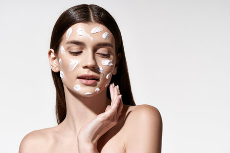 A captivating young woman with delicate white cream adorning her face, exuding beauty and grace.の写真素材