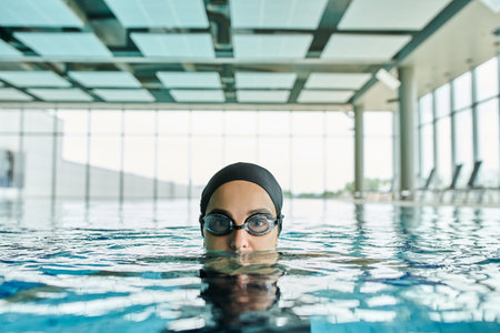 Young woman glides through pool in goggles and swim cap, embodying fluid motion and tranquility.の写真素材