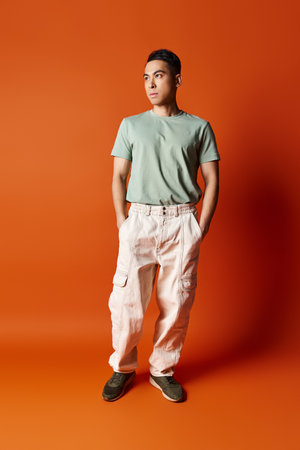 A handsome Asian man stands confidently in stylish attire against a bright orange background in a...