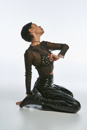 A woman with tattoos sits on the ground, hands on hips, exuding confidence and strength in a studio setting.の写真素材