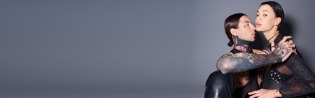 A stylish, tattooed man and woman posing confidently for a portrait in a studio against a grey background.の写真素材