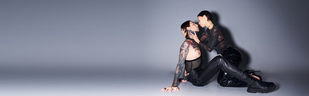 A stylish, tattooed young woman sits gracefully on the ground near man in a studio setting against a grey background.の写真素材