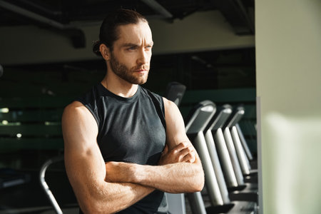 An athletic man in active wear stands confidently in front of a row of treadmills in a gym setting.の写真素材