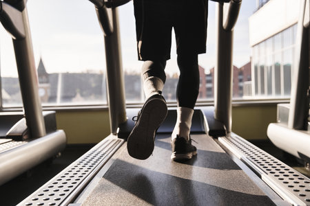 An athletic man in activewear walks briskly on a treadmill at the gym, focusing on his workout...