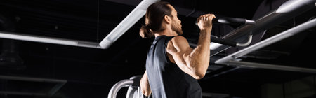 An athletic man in active wear is doing exercises on a pull-up bar in a gym.