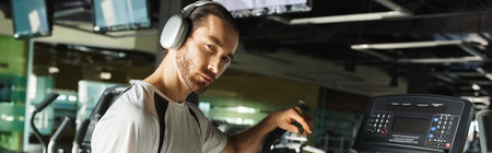 An athletic man in active wear is using a machine while wearing headphones for a music-enhanced...
