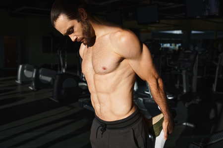 A muscular man without a shirt working out intensely in a gym, showcasing his strength and...