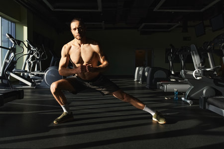 Muscular man without shirt doing a squat exercise in a gym with determination and focus.の写真素材