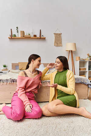 Two teenage girls in casual clothes sitting on the floor engaged in a deep conversation at home.の写真素材