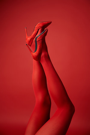 A young woman showcases her legs in tights against a bold red background, exuding strength and confidence.の写真素材