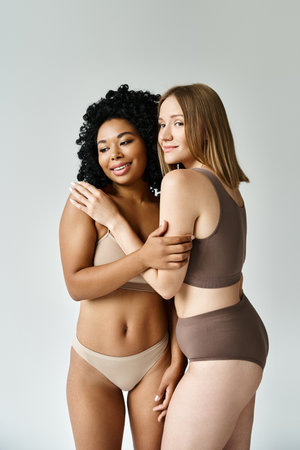 Two beautiful diverse women in cozy pastel underwear pose gracefully for a picture.の写真素材