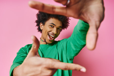 A cheerful young African American man in casual wear on a pink background makes a gesture with his hands, displaying various emotions.の写真素材