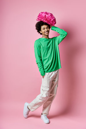 A cheerful young African American man in a green shirt and white pants, with a pink flower on his...