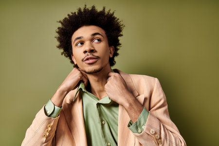 A stylish young African American man with curly hair, wearing a suit jacket and a green shirt, poses...