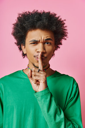 Curly African American man in casual wear looks pensive, with finger in mouth, against pink...