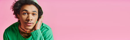 Astonished young African American man with curly hair wearing casual attire, displaying a surprised expression on a pink background.の写真素材