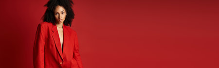 A stylish young woman in a red suit is confidently standing in front of a vibrant red wall.の写真素材