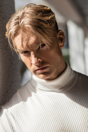 A handsome blonde man in a white turtleneck poses on a Florida street.の写真素材