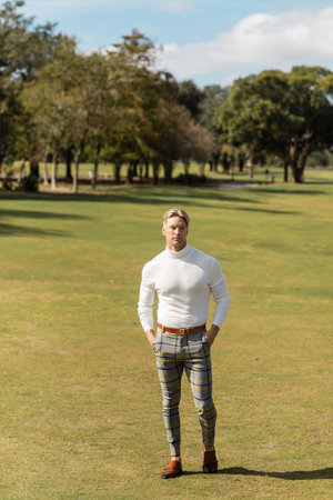 A handsome blonde man in stylish attire walks through a green park in Miami.の写真素材