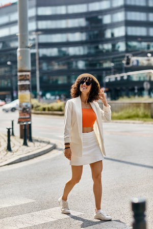 A woman in a white blazer and skirt walks through a European city street.の写真素材