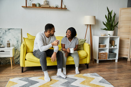 A loving African American couple sits on a yellow couch, enjoying coffee together in their home.の写真素材