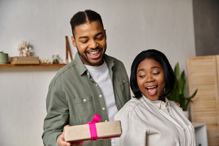 A happy African American couple celebrating at home with a gift.の写真素材