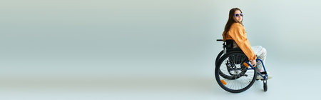 A young woman in a wheelchair poses in a studio setting, wearing a stylish casual outfit and sunglasses.の写真素材