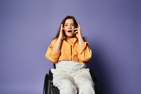 Young woman in casual attire, in wheelchair, sits in studio against purple backdrop, looking surprised with hands over mouthの写真素材