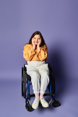 A young woman in casual clothes smiles in a wheelchair, touching her face with both hands. The background is purple and elegantの写真素材