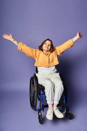 A young woman in a wheelchair sits against a purple background, with her arms raised in a gesture of joy and freedom.の写真素材