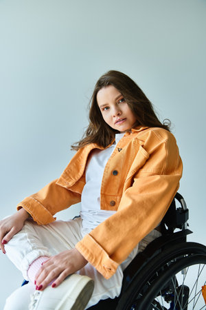 A stylish young brunette woman in a wheelchair poses confidently in a studio setting against a grey...