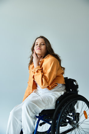 A young woman with long brown hair sits in a wheelchair, wearing a stylish orange jacket and white pants, against a grey backdrop.の写真素材