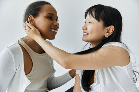 A Black and Asian woman share a tender moment together on a grey backdrop, showing love and affectionの写真素材
