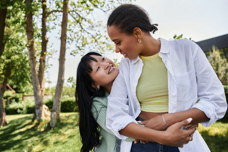 A young lesbian couple embraces and smiles at each other during a sunny outdoor date
