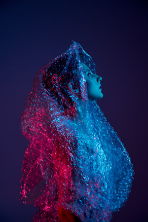 Woman in neon-lit room, head tilted back, wrapped in bubble wrapの写真素材