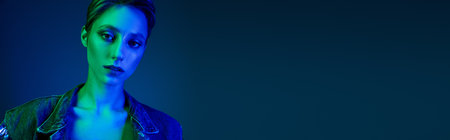 A woman in denim stares pensively into the camera, bathed in a blue and green light.の写真素材