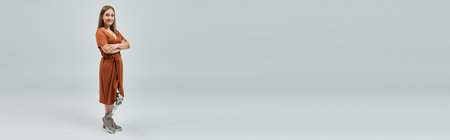 A woman with a prosthetic leg stands confidently with arms crossed, wearing a copper dress.の写真素材