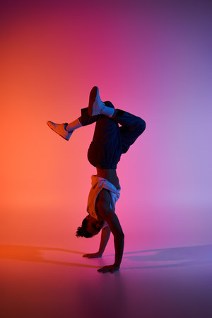 A young African American man performs a handstand against a colorful, gradient background.