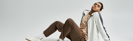 A young African American man in a stylish white jacket and brown pants poses against a grey background.の写真素材