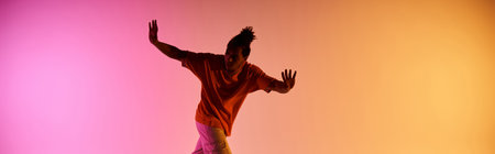 A young African American man dances in front of a pink and orange gradient background.の写真素材
