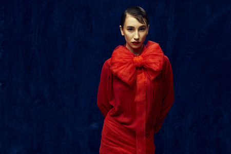 A young woman with short hair poses against a blue backdrop, wearing a red dress with a large bow.の写真素材
