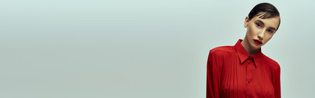 A young woman with short hair poses against a grey background. She wears a red blouseの写真素材