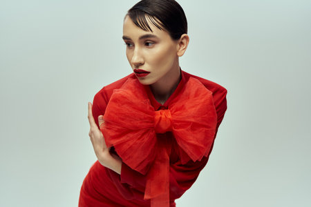 A young woman with short hair poses in a striking red outfit featuring a large bow against a grey backdrop.の写真素材