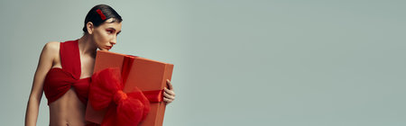 A young woman with short hair, wearing a red outfit with a large bow, holds a gift in a studio setting.の写真素材