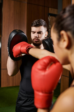 A woman in a black shirt and red boxing gloves trains in a gym.の写真素材
