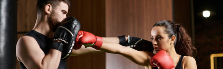 A male trainer guides a brunette sportswoman in active wear as they engage in a boxing session in a gym.の写真素材