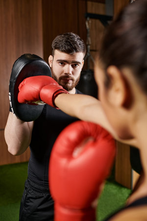 A woman in a black shirt and red boxing gloves practices boxing in a gym.の写真素材