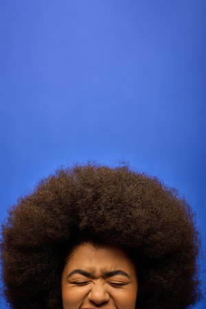 Stylish African American woman with curly hairdohairdo posing against a vibrant blue backdrop.の写真素材