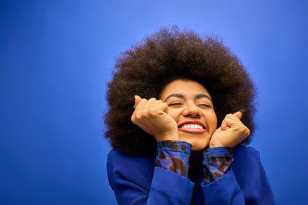 A stylish African American woman with curly hairdosmiles and holds her hands up in front of her face in a joyful pose.の写真素材